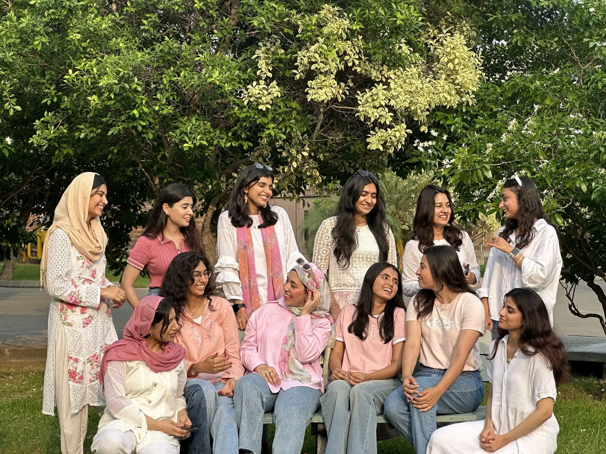 The women of SPADES, dressed in pink and white, around a bench under flowering trees.